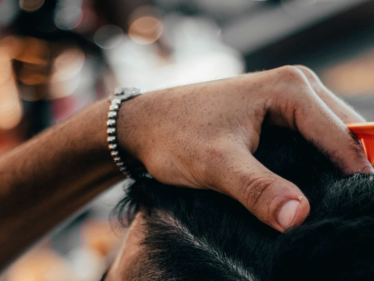 Zbliżenie dłoni barbera przycinających włosy na boku głowy klienta