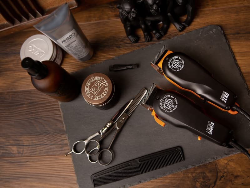 Maszynki do strzyżenia, nożyczki, grzebień i kosmetyki barberskie ułożone na kamiennej płycie