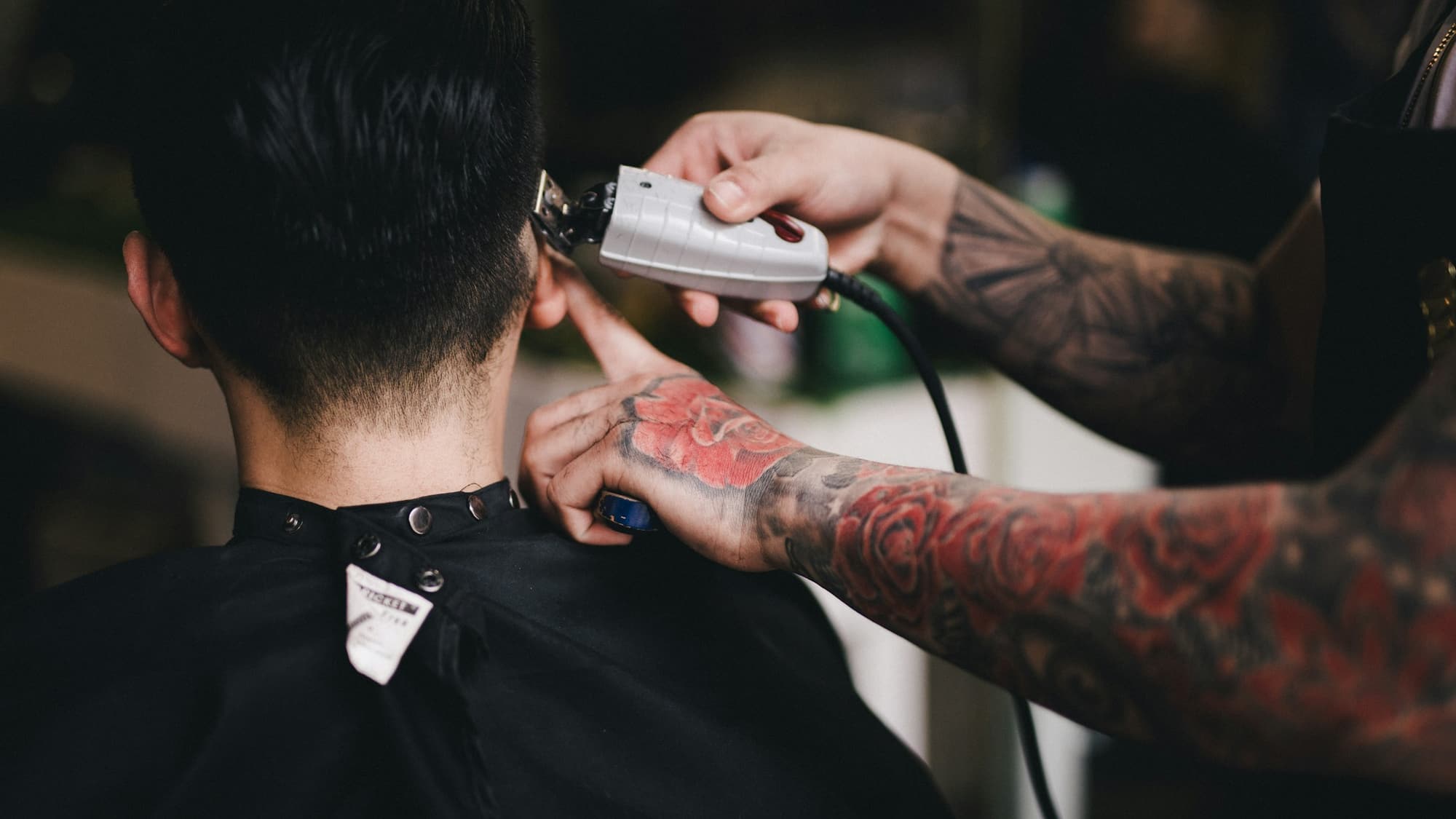 Barber wykańcza maszynką linię włosów na karku klienta siedzącego w fotelu fryzjerskim